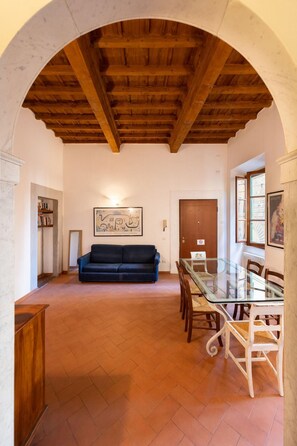 A spacious room with a wooden ceiling, a glass dining table with chairs, a dark blue sofa, and a bookshelf. - Acqua Apartment in Firenze (Florence)