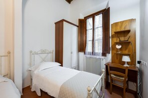 A bedroom with a bed, a wooden desk, a chair, a radiator, and a window with curtains. - Acqua Apartment in Firenze (Florence)