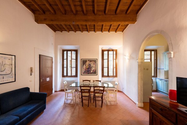 A spacious living area with a wooden ceiling, a dining table with chairs, a sofa, and a television on a wooden cabinet. - Acqua Apartment in Firenze (Florence)