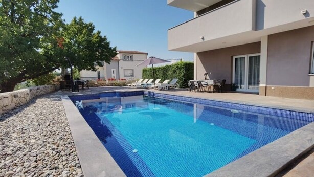 Una piscina con sillas de descanso y una mesa, rodeada por un muro de piedra y un edificio con balcón.