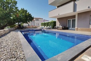 En swimmingpool med solstolar och ett bord, omgiven av en stenmur och en byggnad med en balkong.
