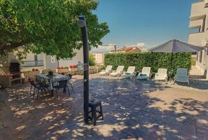 Terrassa exterior amb taula i cadires, una barbacoa i un gran parasol.