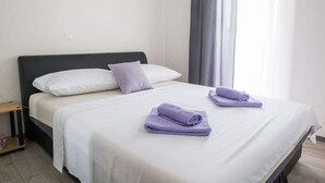Una cama bien hecha con ropa blanca y dos toallas moradas dobladas.