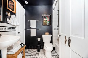 Een badkamer met een zwart-wit betegelde vloer, een wit wastafelmeubel, een toilet en een lijst met een foto aan de muur.