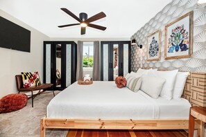 A bedroom with a bed, a ceiling fan, a TV, and a window with curtains.