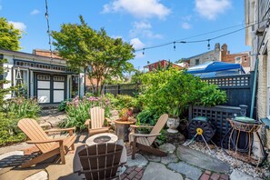 A patio with Adirondack chairs, a table, and a garden with various plants and flowers. - Garden Retreat on Carroll Creek + Free Parking (Frederick)