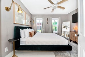 Une chambre à coucher avec un lit, un ventilateur de plafond, des lampes de chevet et une vue sur l’extérieur.