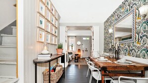A dining area with a wooden table, white chairs, a patterned wall, and a staircase.