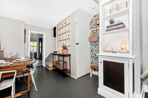 A dining area with a wooden table set for four, a white chair, and a small bench. There is a white cabinet with a glass top and a shelf above it. - Garden Retreat on Carroll Creek + Free Parking (Frederick)