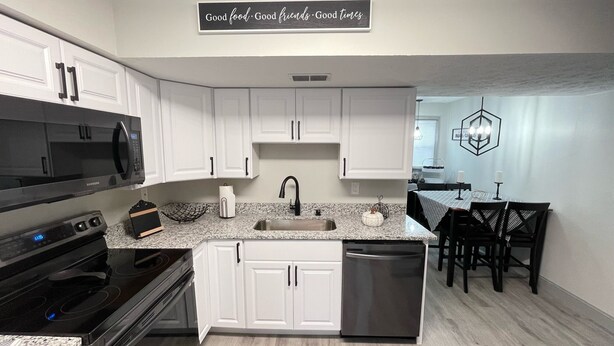 A modern kitchen with white cabinets, a black microwave, and a stainless steel dishwasher. There is a sign above the sink that reads "Good food. Good friends. Good times." - 1st Floor Completely Remodeled, Pets Welcome!!! King & Queen Beds, W/D in Unit., (Monroe)