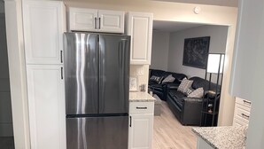 A modern kitchen with white cabinetry, a stainless steel refrigerator, a granite countertop, and a black leather sofa in the adjacent living area. - 1st Floor Completely Remodeled, Pets Welcome!!! King & Queen Beds, W/D in Unit., (Monroe)