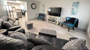 A living room with a sectional sofa, a TV on a stand, a ceiling fan, and a kitchen in the background. - 1st Floor Completely Remodeled, Pets Welcome!!! King & Queen Beds, W/D in Unit., (Monroe)