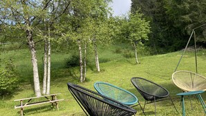 Un espacio al aire libre con césped, un banco de madera y cuatro sillas.