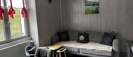A cozy room with a grey sofa, a small table, and a window with red curtains.