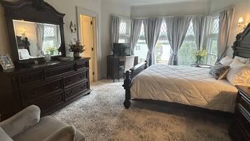 Een slaapkamer met een groot bed, een dressoir, een kaptafel met spiegel en een televisie.