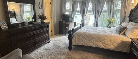 Une chambre à coucher avec un grand lit, une commode, une coiffeuse avec un miroir et un téléviseur.
