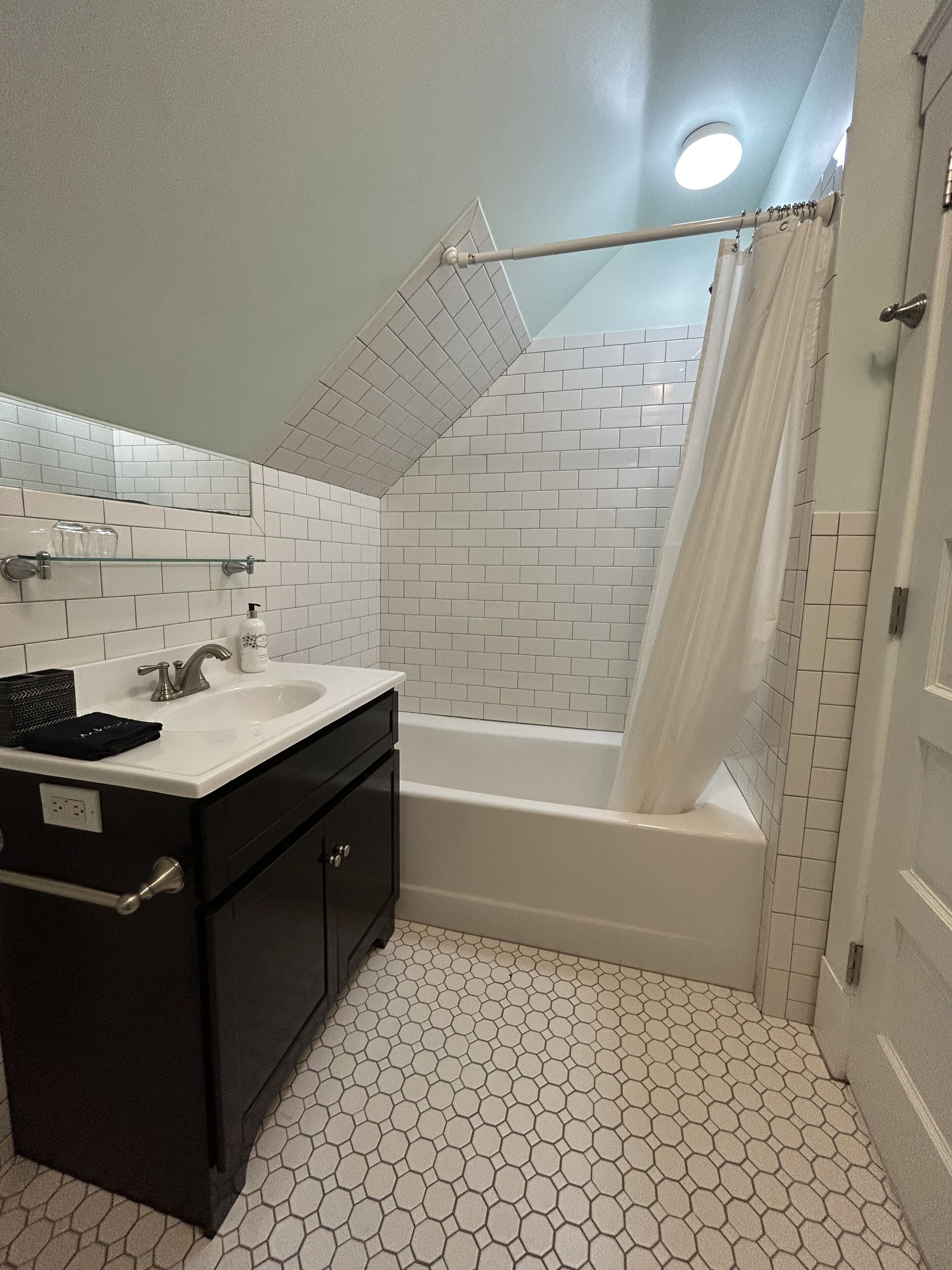 Un baño con una bañera blanca, un tocador negro y una cortina de ducha.