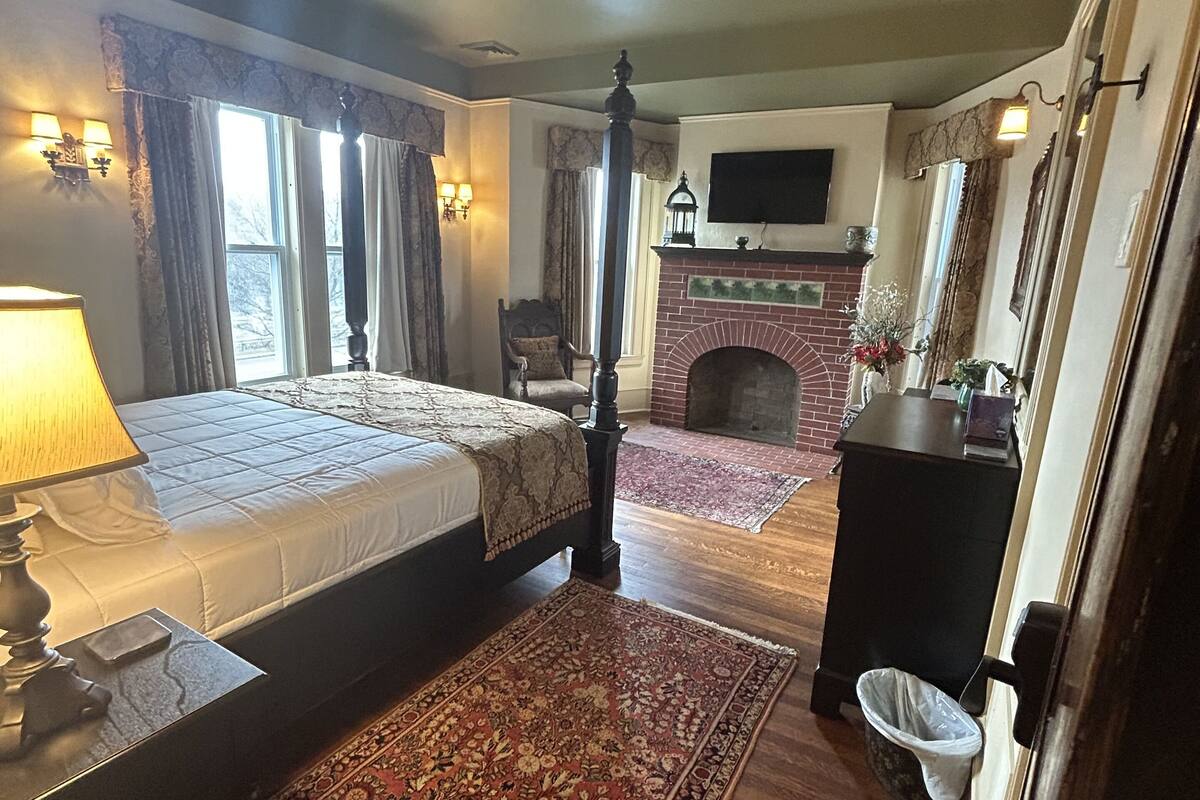 A bedroom with a four-poster bed, a fireplace, and a large rug.