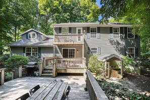 Une maison à deux étages avec une terrasse, un barbecue et un petit abri de jardin.