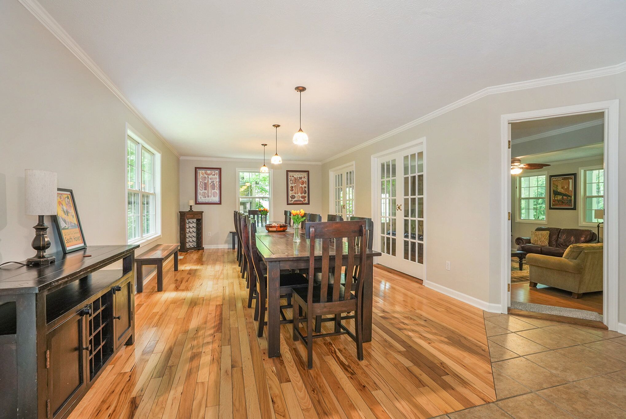 A spacious dining area with a long wooden table and chairs, a bench, and pendant lighting.