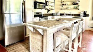 A kitchen with a stainless steel refrigerator, a microwave, a stove, and a sink. There is a wooden island with bar stools. - Little Pipestone Lodge w/ Views (Whitehall)