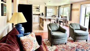 A cozy living room with a sofa, two armchairs, a lamp, and a rug. A kitchen and dining area are visible in the background. - Little Pipestone Lodge w/ Views (Whitehall)