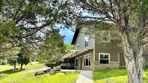 A house with a covered patio, a stone foundation, and a well-maintained lawn. - Little Pipestone Lodge w/ Views (Whitehall)