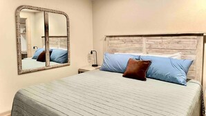 A bedroom with a large bed, a wooden headboard, a nightstand with a lamp, and a mirror on the wall. - Little Pipestone Lodge w/ Views (Whitehall)