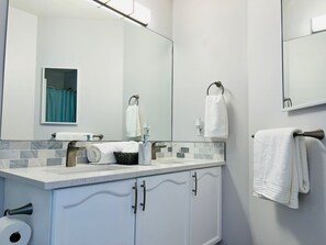 Une salle de bain moderne avec un grand miroir, un lavabo blanc, un porte-serviettes et un support à papier toilette.