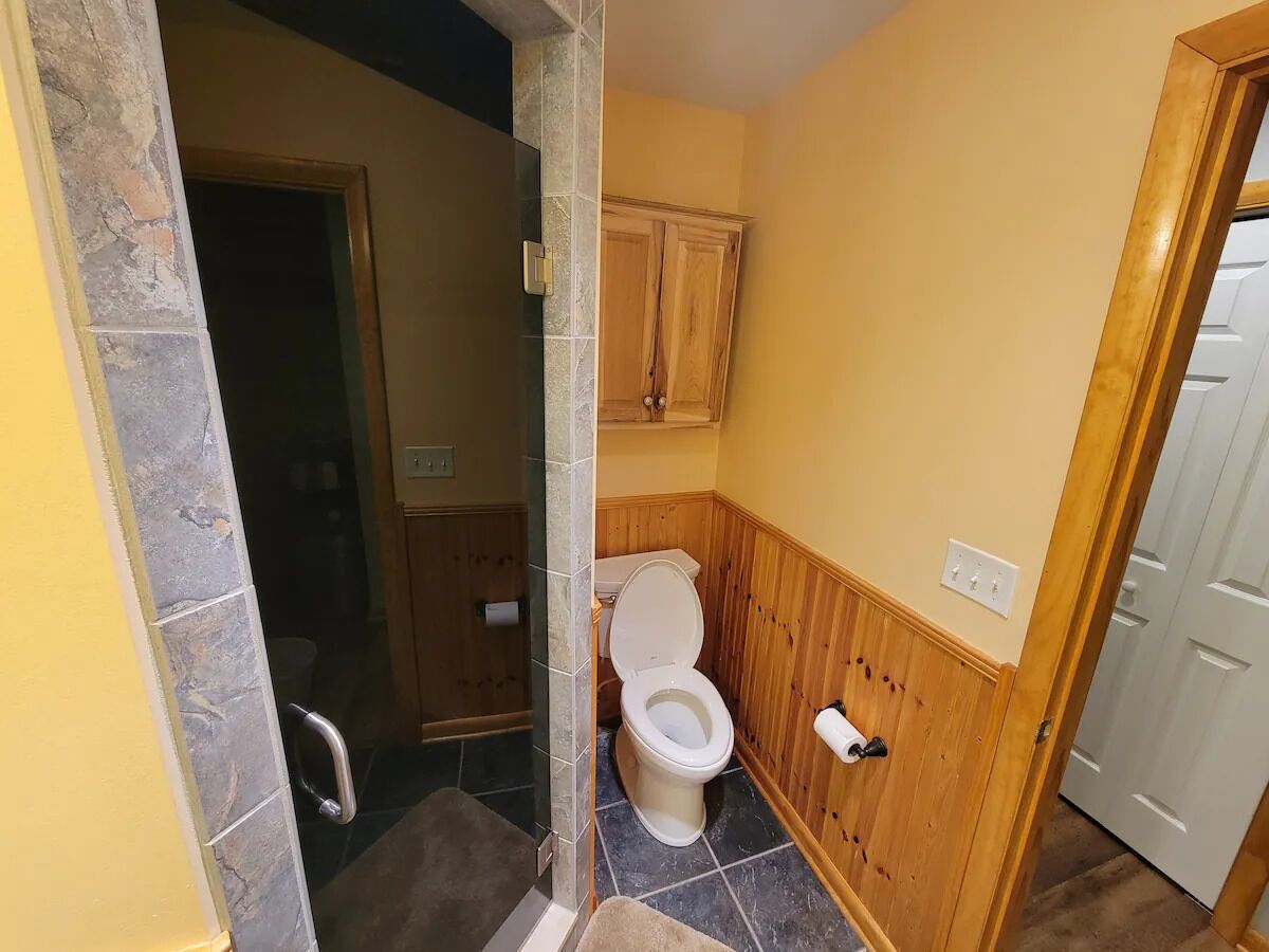 A bathroom with a toilet, wooden vanity, and a shower area.