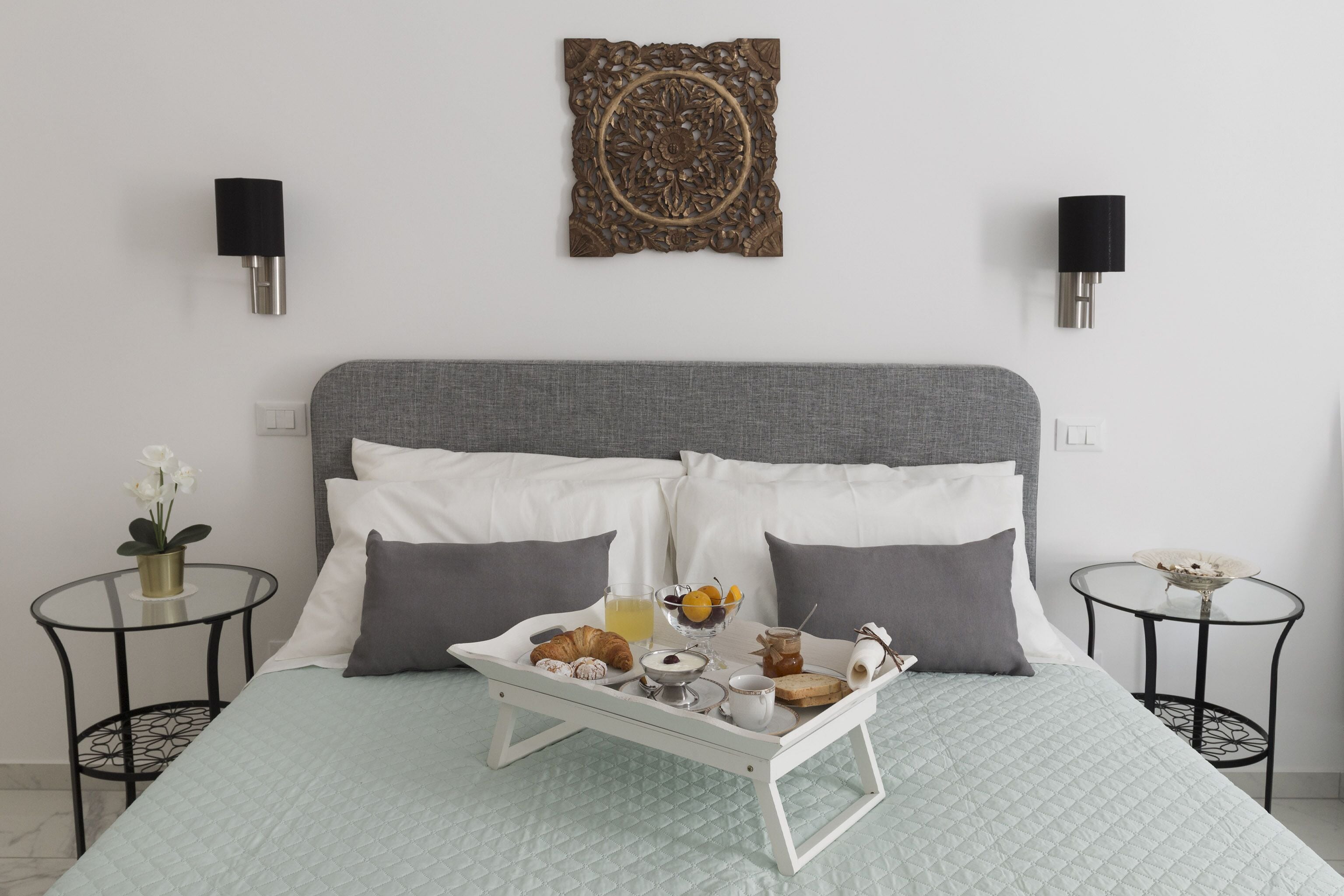 Un lit bien fait, avec un plateau contenant des éléments de petit-déjeuner, deux tables de chevet et un élément décoratif mural.