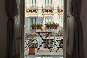 An open balcony with a table and chairs, potted plants, and a view of a building with balconies and windows. - Calafatari B&B (Syracuse)