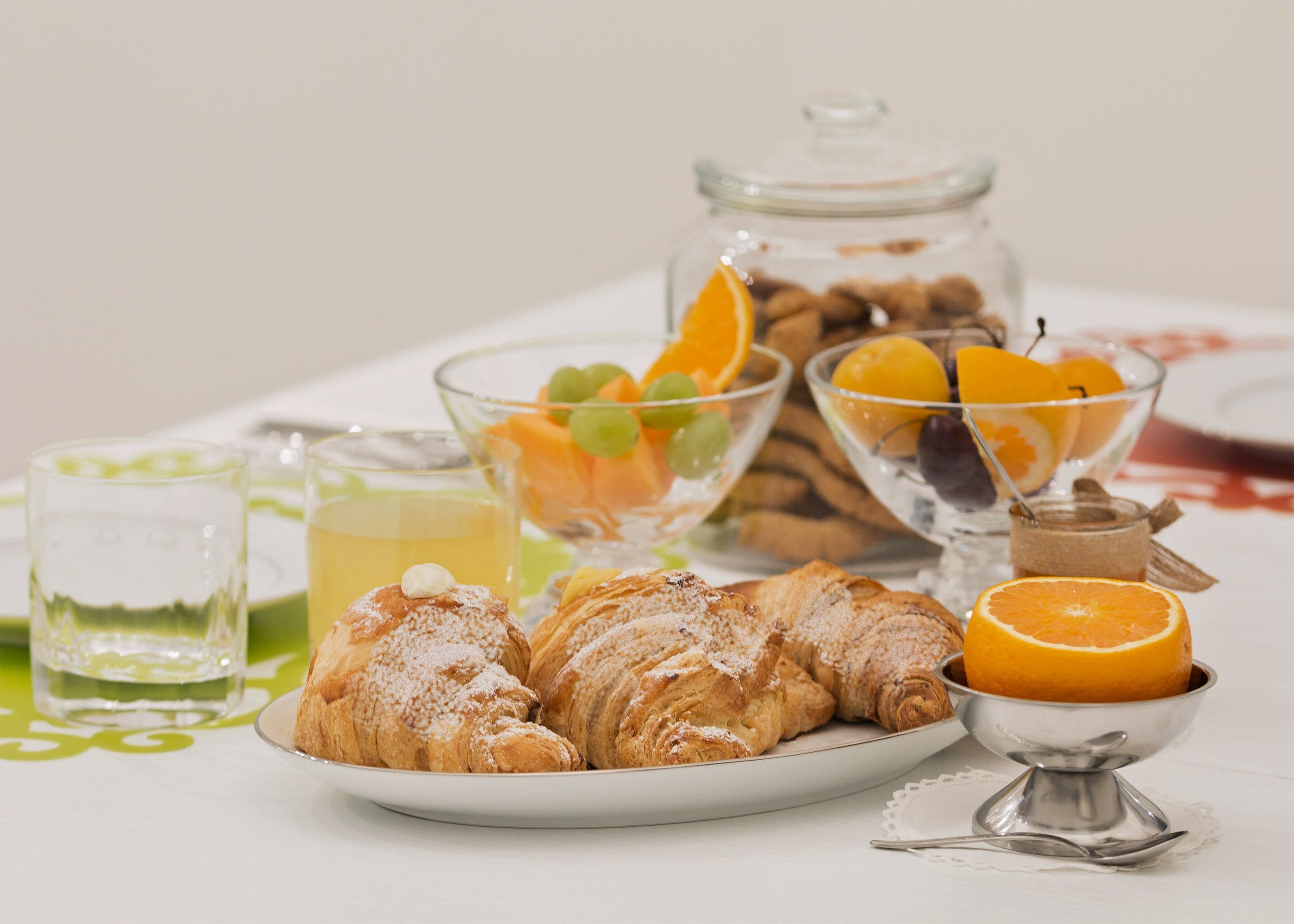A breakfast setting with croissants, fruit, and a glass of juice on a table.