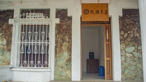 A hotel entrance with a wrought iron gate, a stone wall, and a wooden door with a sign above it. - NATZ HOTEL (Flores)