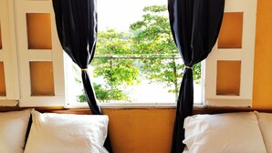 A room with two beds, a window with curtains, and a view of greenery outside. - NATZ HOTEL (Flores)