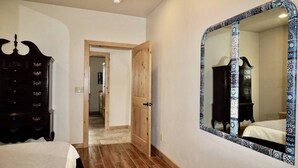 A bedroom with a wooden wardrobe, a large mirror with a patterned frame, and a door leading to another room.