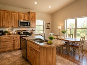 A kitchen with wooden cabinets, a central island, stainless steel appliances, and a dining area with a table and chairs. - Upper Ranch - 100 Acre Mountain Views (Whitehall)