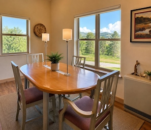A dining room with a wooden table, four chairs, two floor lamps, a potted plant, and large windows with a view of greenery. - Upper Ranch - 100 Acre Mountain Views (Whitehall)