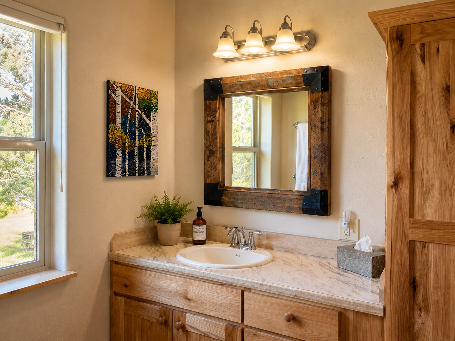 A bathroom with a wooden vanity, a sink, a mirror with a rustic frame, and a wall-mounted light fixture.