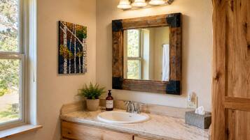 A bathroom with a wooden vanity, a sink, a mirror with a rustic frame, and a wall-mounted light fixture.