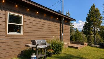 A house with a wooden exterior, a window, a barbecue grill, and a propane tank.