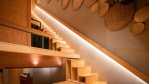 Un escalier en bois, avec un plafond en pente et des paniers tressés accrochés au mur.
