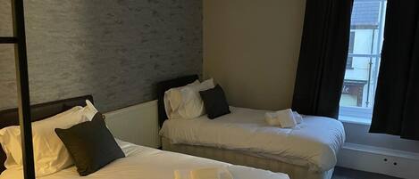 A hotel room with two beds, a window with curtains, and a view of the outside.