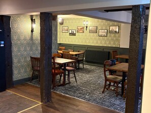 A restaurant interior with patterned wallpaper, wooden tables and chairs, and framed pictures on the wall. - St Ives (Neath)