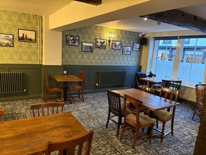 Un interior de restaurante con mesas y sillas de madera, papel tapiz estampado y cuadros en las paredes.