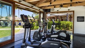 Ein überdachter Fitnessbereich mit Cardiogeräten, großen Fenstern und Blick auf den Außenpool.