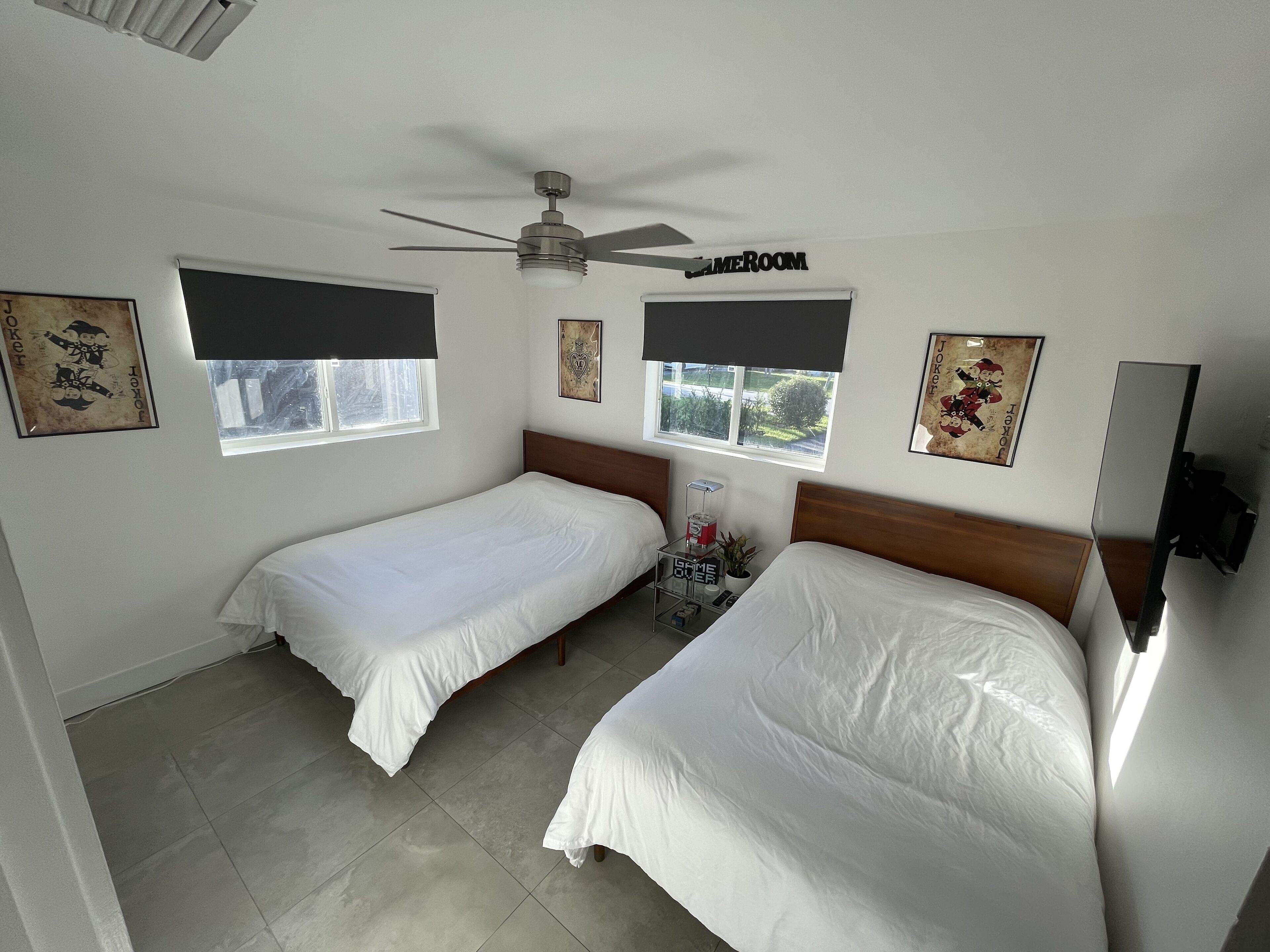 A hotel room with two single beds, a ceiling fan, a window with a view, and artwork on the walls.