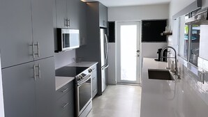 A modern kitchen with grey cabinets, stainless steel appliances, and a white countertop. - Modern lakeside pool home near hardrock and fll airport  (Davie)