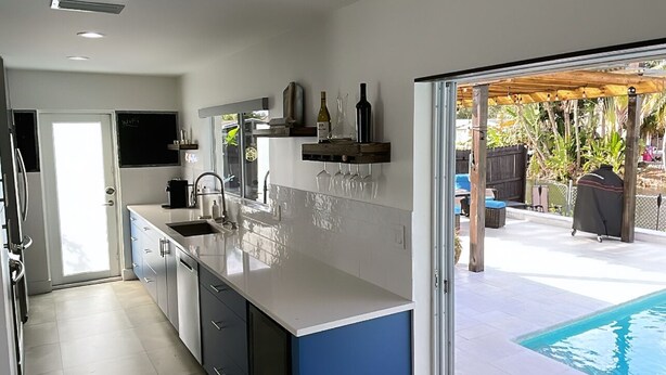A modern kitchen with a large island, a built-in oven, and a sink. There is a sliding glass door leading to a pool area. - Modern lakeside pool home near hardrock and fll airport  (Davie)