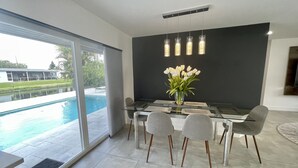 A modern dining area with a glass table, grey chairs, and a vase of white flowers. - Modern lakeside pool home near hardrock and fll airport  (Davie)